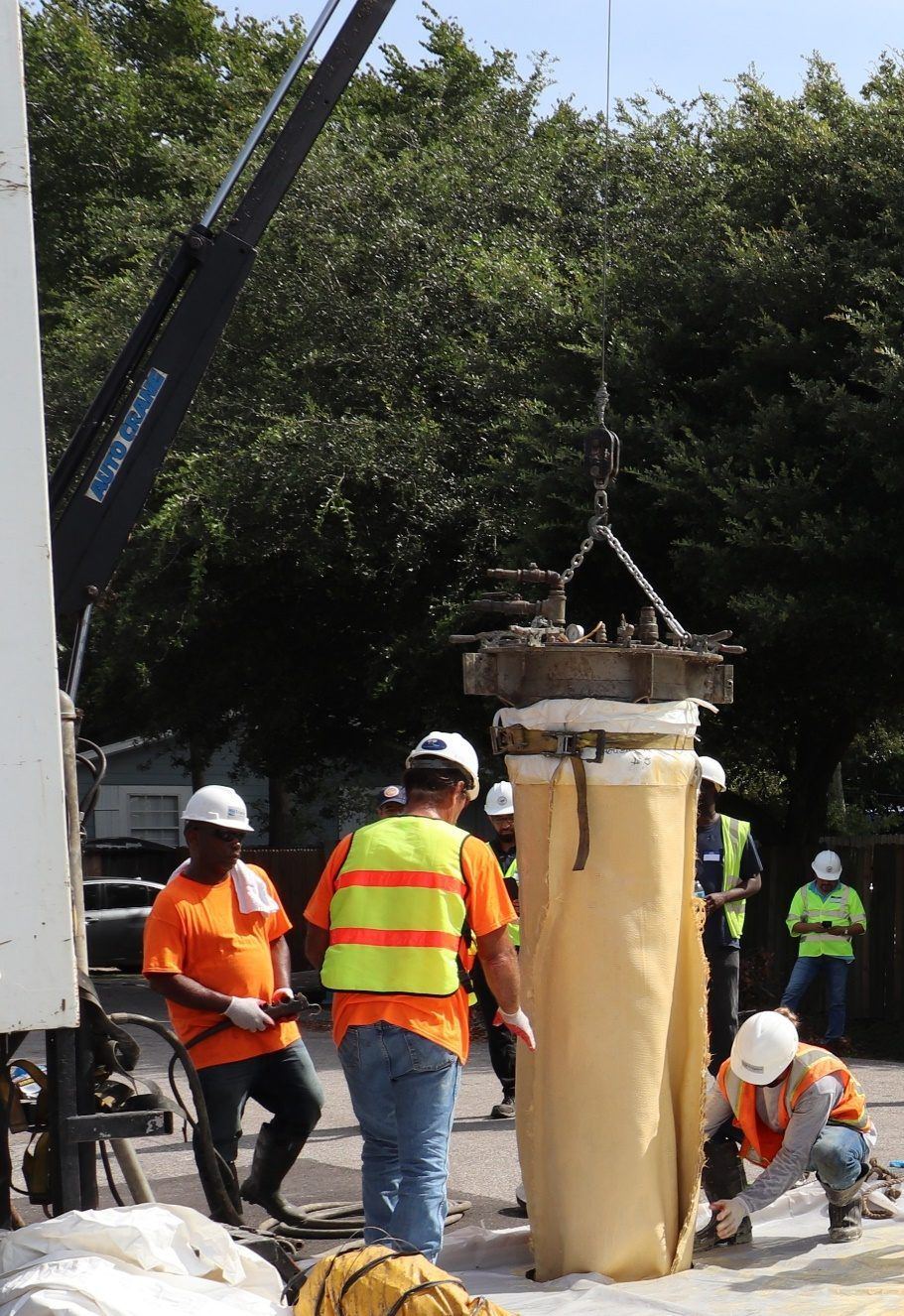 A crew lowering a saturated Triplex Liner into a manhole from a crane