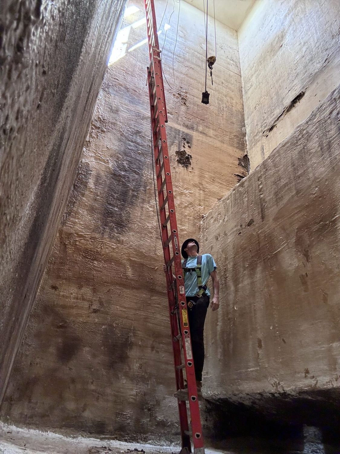 A West Texas lift station before lining, bare corroded concrete, with a man on an extension ladder for scale